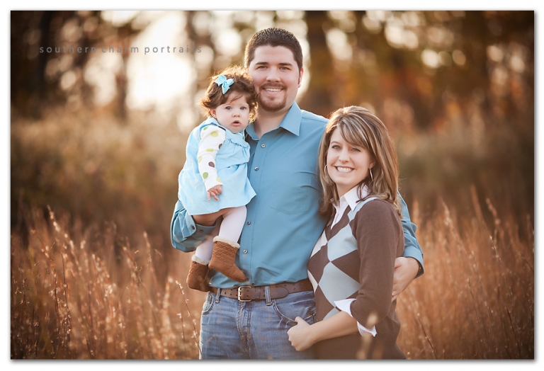 family of three in field together for fall family portraits wearing beautiful browns and blues