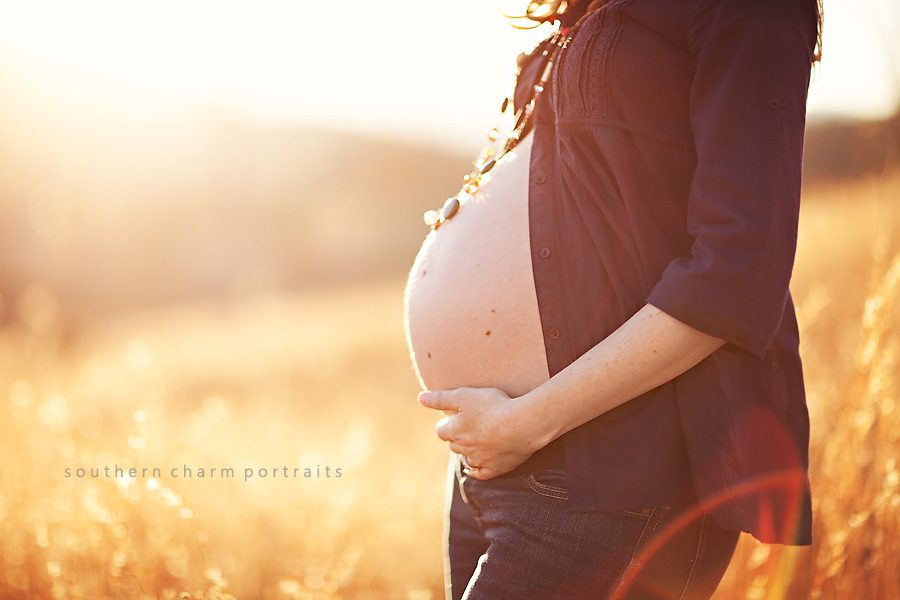 pregnant belly with stone necklace against the afternoon sunlight