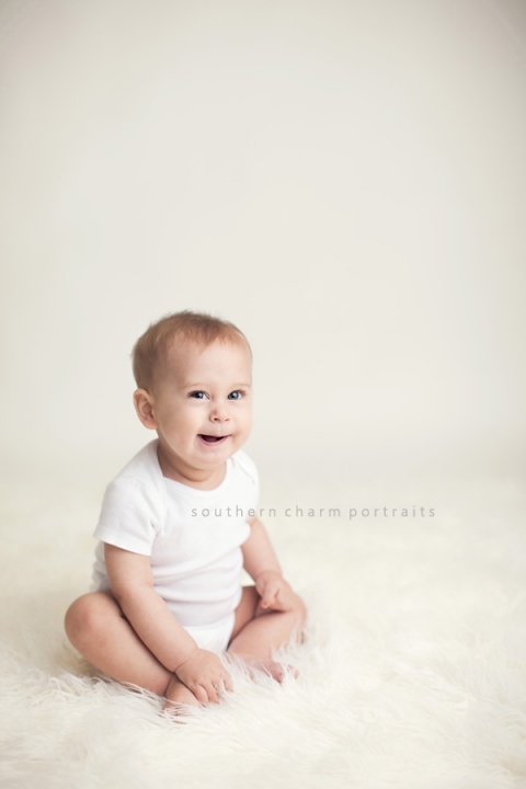 baby boy sitting in white onesie with sweet grin on face