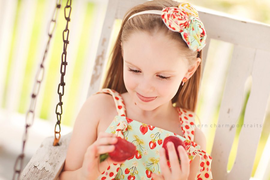 little girl on porch swing eating fresh strawberries