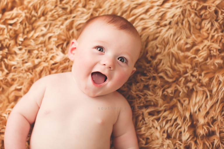 baby laying on brown blanket smiling really big